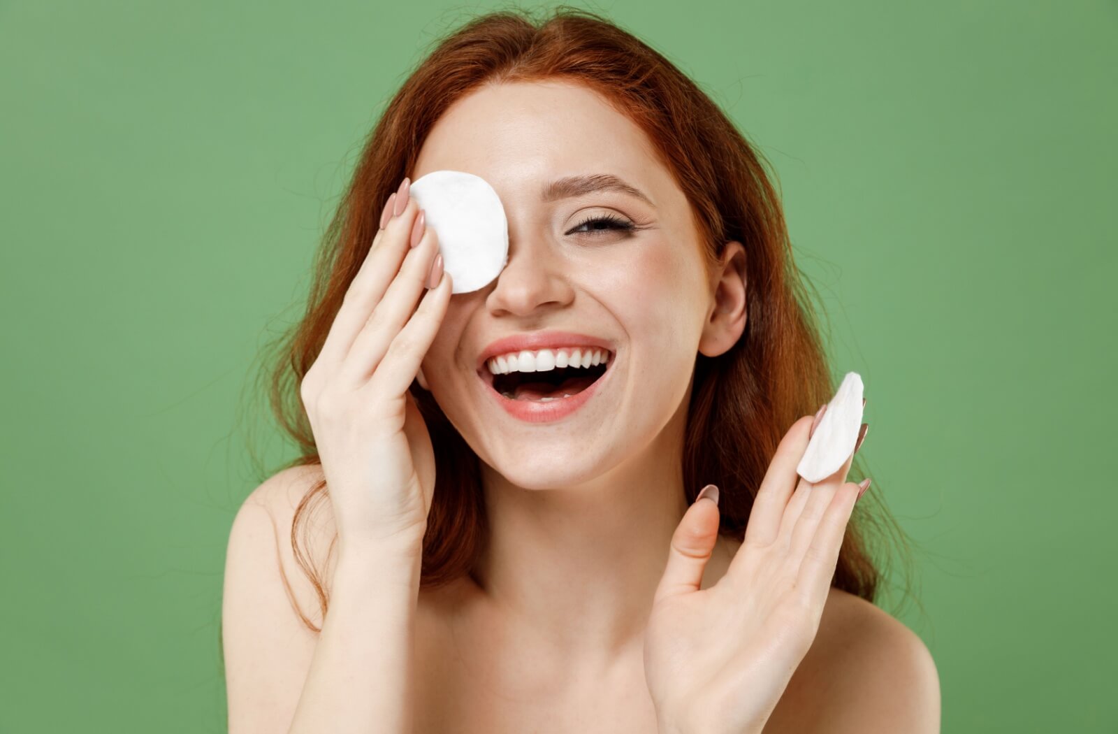 A person with a cheerful smile covers their left eye with a cotton round.