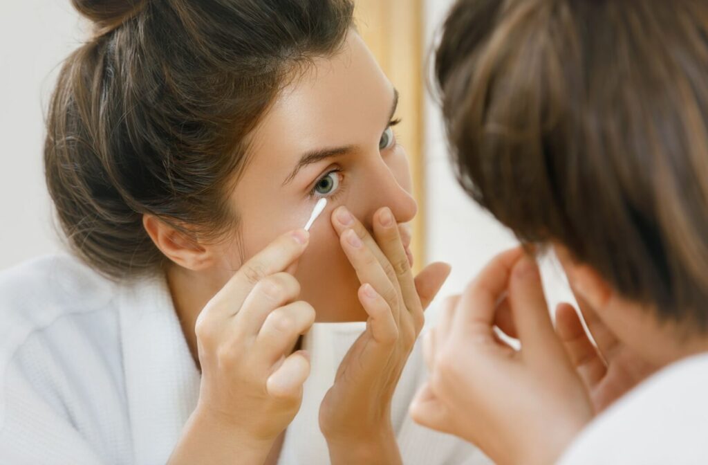 A person carefully uses a Q-tip to remove their eye makeup.