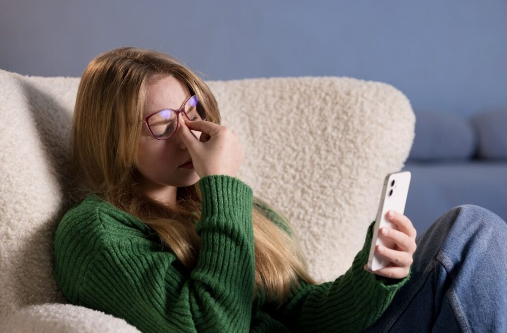 A person in a green sweater holding a smartphone while rubbing their eyes, showing how eye fatigue and digital eye strain can lead to dizziness.