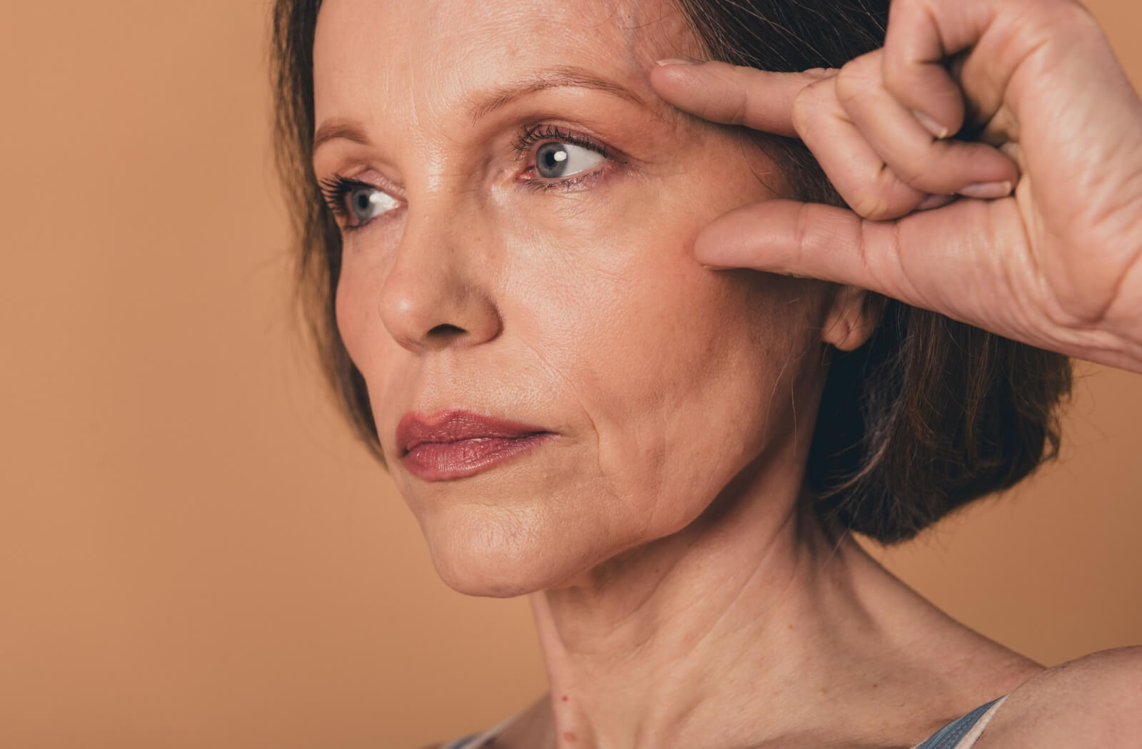 A person pointing to wrinkles around their eyes, demonstrating common skin aging concerns and the need for anti-aging eye treatments.