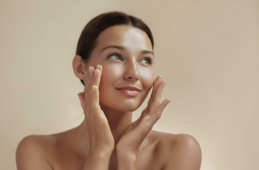 A person smiling and applying skincare products to their face, highlighting youthful skin and the benefits of effective eye wrinkle treatments.